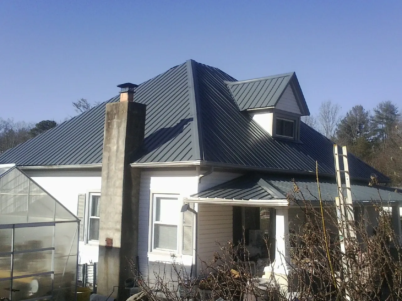 Dark blue standing seam metal roof on a white farmhouse with dormer — Slate & Tile Roof Repair by Roofing Brothers in Carver