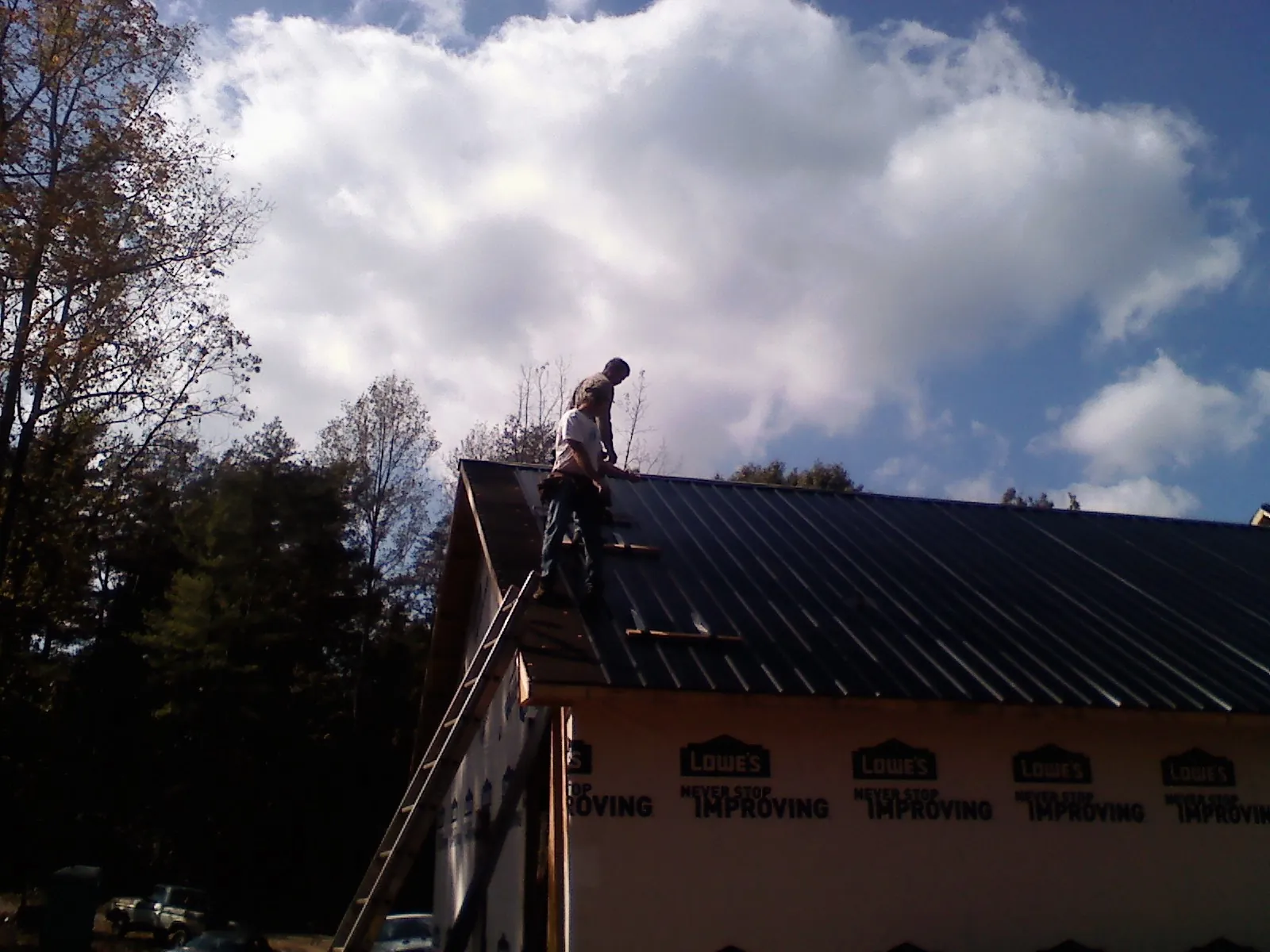 Roofer fastening dark metal panels high against a cloudy sky, from a Roof Inspection job in Carver