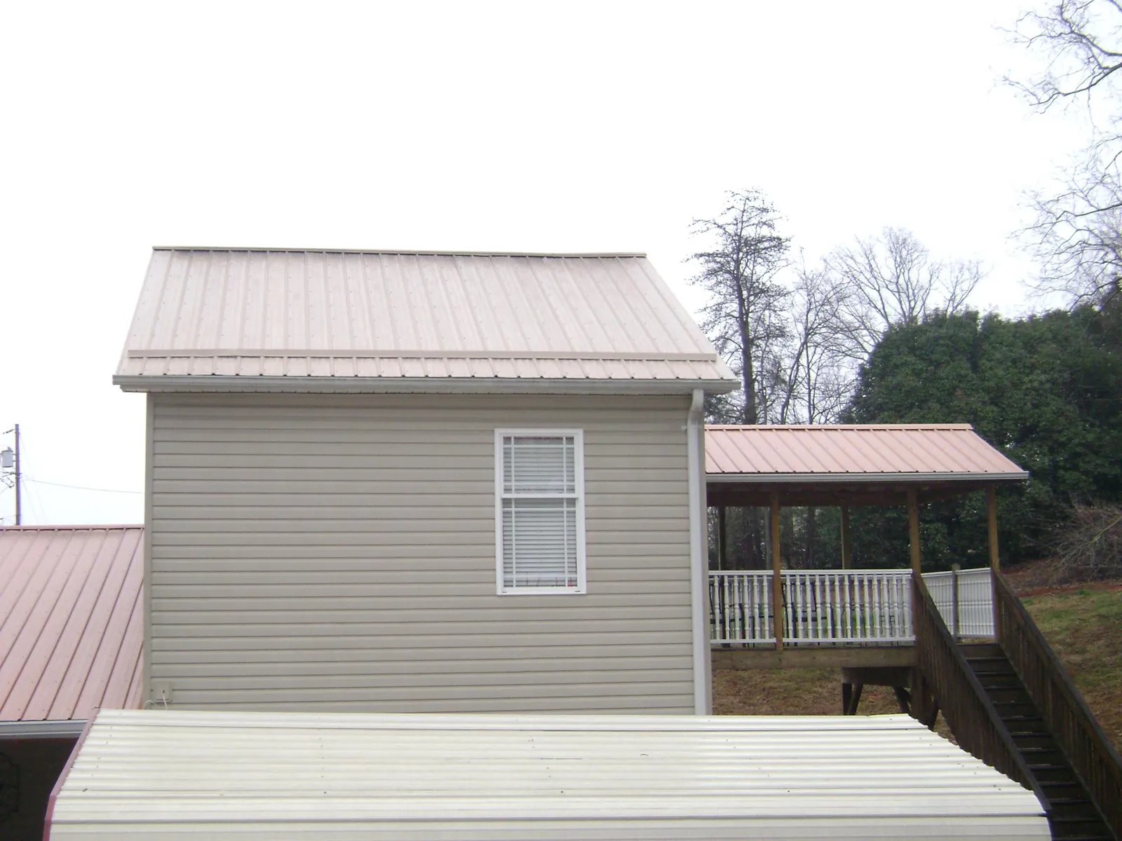 Tan metal roofs on a two story addition and attached porch, from a Roof Replacement job in Carver